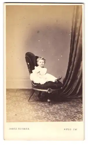 Fotografie Jabez Hughes, Ryde, Isle of Wight, Kleinkind im strahlend weissen Gewand in einem edlen Sessel sitzend