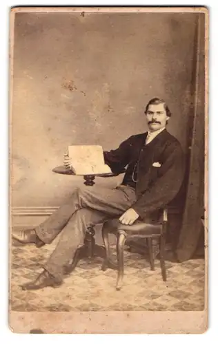 Fotografie unbekannter Fotograf und Ort, Junger Herr mit gepflegtem Mousatche in lässiger Pose auf einem Stuhl sitzend