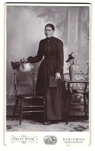 Fotografie Fritz Ette, Eisleben, Bahnhofstrasse 18, Junge Frau im eleganten Kleid neben einen Stuhl stehend