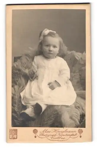Fotografie Max Hinzelmann, Cottbus, Baby im eissen Kleidchen auf Fell sitzend