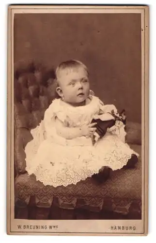 Fotografie W. Breuning, Hamburg, Berg-Strasse 26, Baby in weissem Kleidchen mit Puppe in der Hand