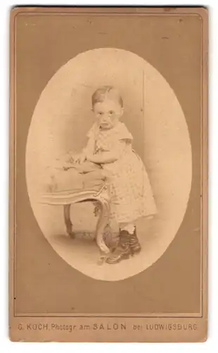 Fotografie G. Koch, Ludwigsburg, Am Salon, Kleinkind im kariertem Kleid mit Lederstiefeln