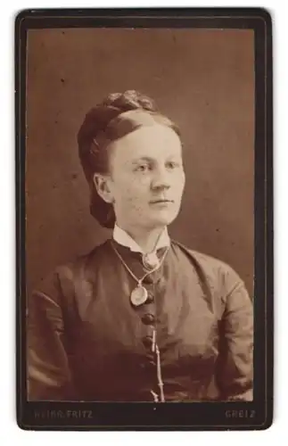 Fotografie Heinrich Fritz, Greiz, Dame mit Duttfrisur, Brosche und grossem Medaillon