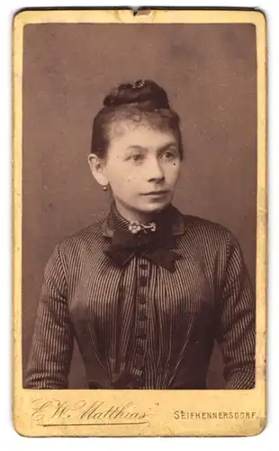 Fotografie E. W. Matthias, Seifhennersdorf, Junge Dame mit Hochsteckfrisur im gestreiften Kleid mit Schleife am Kragen