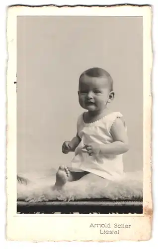 Fotografie Arnold Seiler, Liestal, Süsses Kleinkind im Hemd sitzt auf Fell