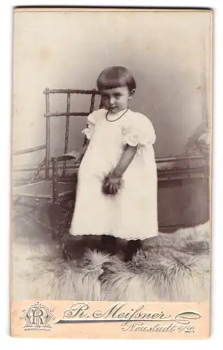 Fotografie R. Meissner, Neustadt a. D., Kleinkind im weissem Kleid an Stuhl abstützend