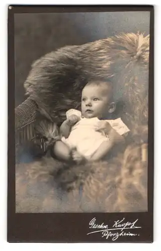 Fotografie Geschw. Knopf, Pforzheim, Süsses Kleinkind im Hemd liegt auf Fell