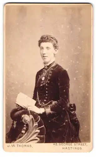 Fotografie J. W. Thomas, Hastings, 45. George Street, Dame in Samttournüre und Buch in der Hand