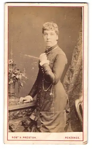 Fotografie Robt. H. Preston, Penzance, Frau im Kleid mit Kette sich auf einen Tisch stützend