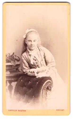 Fotografie Arthur Reston, Stretford, 6 Dorset Street, Mädchen mit Haarschleife an einen Stuhl lehnend
