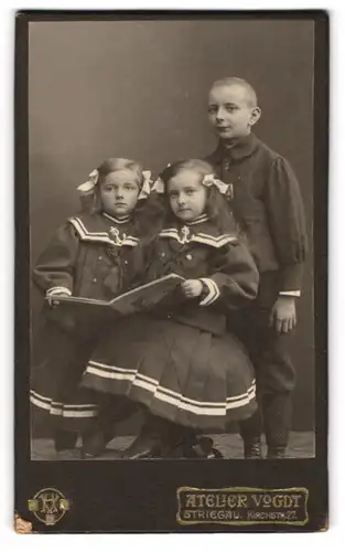 Fotografie Atelier Vogdt, Striegau, Kirchstr. 27, Junger Mann in modischer Kleidung und zwei Mädchen mit Bilderbuch