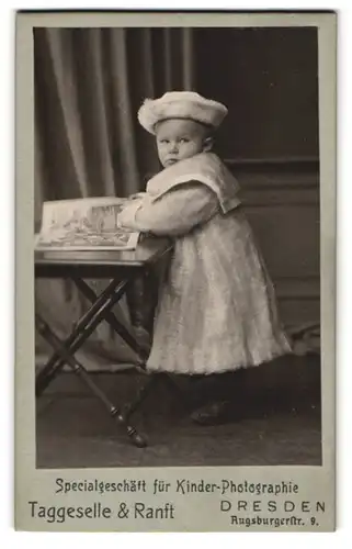Fotografie Taggeselle & Ranft, Dresden, kleines Kind im Wintermantel mit Pelzhut blättert in einem Heft