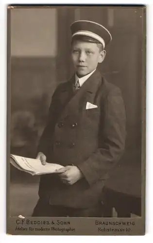 Fotografie C. F. Beddies & Sohn, Braunschweig, junger Knabe als Student im Anzug mit Schirmmütze und Zeitung