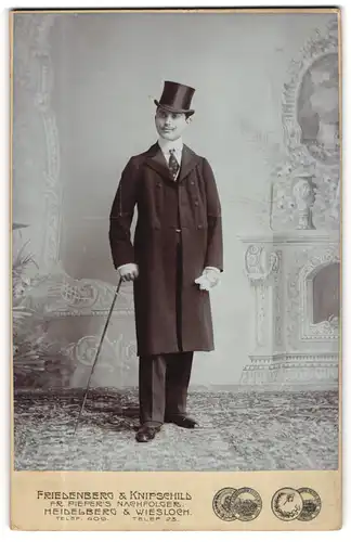 Fotografie Friedenberg & Knipschild, Heidelberg, junger Mann im Anzug mit Mantel trägt Zylinder, Flanierstock