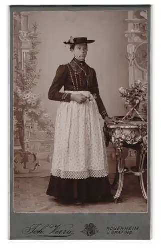 Fotografie Joh. Verra, Rosenheim, Dame im dunklen Kleid mit Schürze und Hut