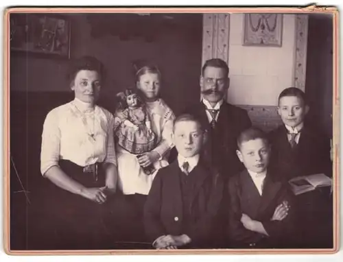 Fotografie unbekannter Fotograf und Ort, Familie im Wohnzimmer mit Puppe im Arm, Kachelofen