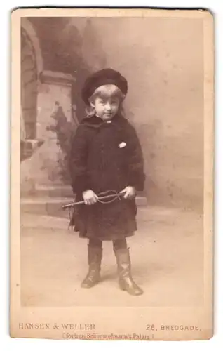 Fotografie Hansen & Weller, Kopenhagen, Bredgade 28, Kleines Mädchen in Hut und Mantel mit Spielpeitsche in der Hand