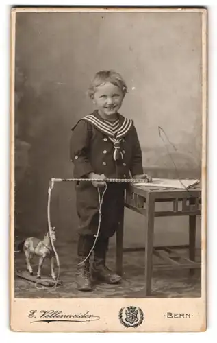 Fotografie E. Vollenweider, Bern, Postgasse 68, Lächelnder kleiner Junge im Matrosenanzug mit Spielzeugpferd