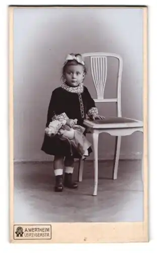 Fotografie A. Wertheim, Berlin, Leipzigerstrasse, Kleines Mädchen mit Haarschleife und Puppe neben einem Stuhl