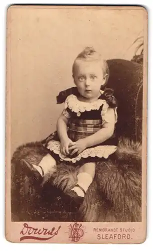Fotografie Downes, Sleaford, Kleines Mädchen im Kleid sitzt auf Fell