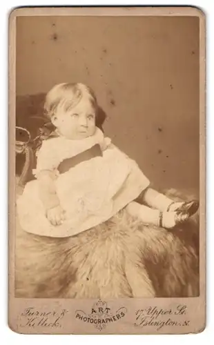 Fotografie Turner & Killick, Islington, 17. Upper Street, niedliches Kleinkind auf einem Fell sitzend