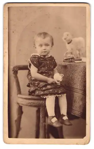 Fotografie unbekannter Fotograf und Ort, Kleinkind mit Kanne nebst Spielzeug auf Stuhl sitzend