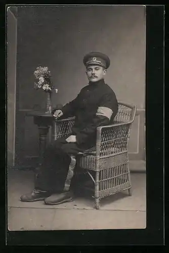 AK Kriegsgefangener mit heller Armbinde und Zigarette in einem Korbsessel