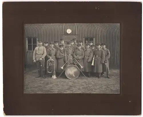 Fotografie unbekannter Fotograf und Ort, Soldaten in Uniform mit Musikinstrumenten vor einer Blechbaracke, Tuba, Oboe