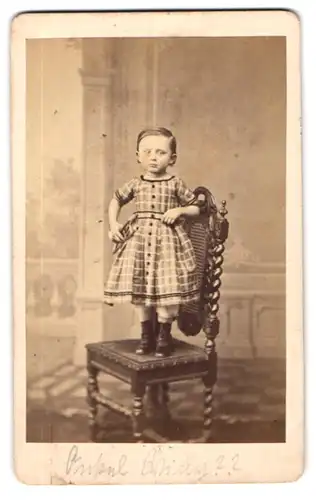 Fotografie G. Kegel, Cassel, Portrait niedliches kleines Mädchen im karierten Kleid posiert stehend auf dem Stuhl