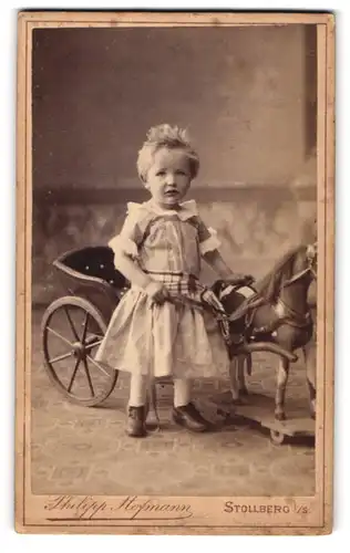 Fotografie Philipp Hofmann, Stollberg i. S., Portrait niedliches Kleinkind im Kleid mit Spielzueg Pferdekutsche