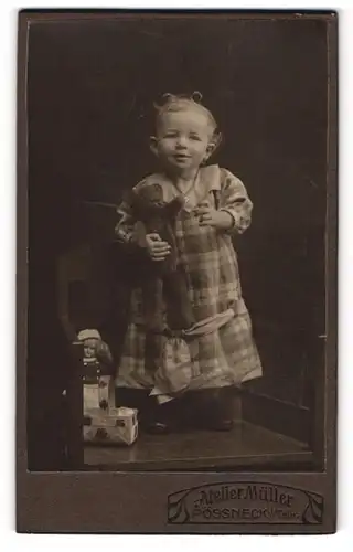 Fotografie Atelier Müller, Pössneck i, Th., Kleinkind im karierten Kleid mit Teddybär im Arm