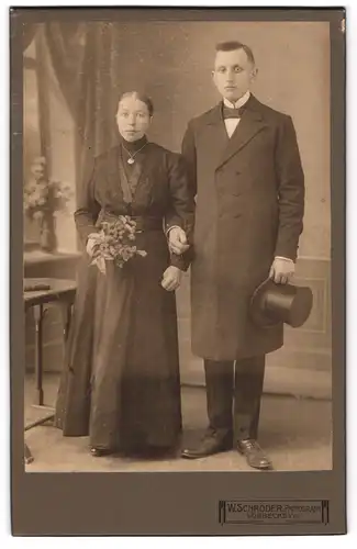 Fotografie W. Schröder, Lübbecke i. W., junges Brautpaar im schwarzen Hochzeitskleid und Anzug mit Zylinder