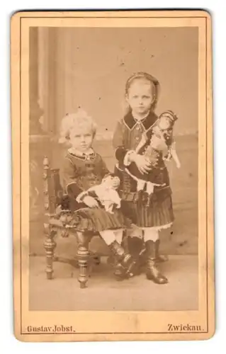Fotografie Gustav Jobst, Zwickau, zwei kleine Mädchen in Kleidern mit ihren Puppen im Arm