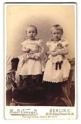Fotografie Rud. Conrad, Berlin, zwei blonde Mädchen in Kleidern mit Puppe und Spielzeugpferd