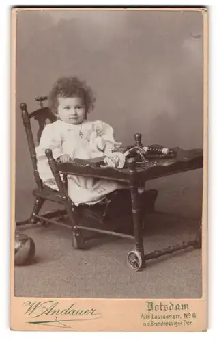 Fotografie W. Andauer, Potsdam, Kleinkind mit Locken im weissen Kleidchen sitzt im Kinderstuhl
