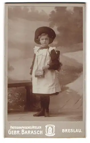 Fotografie Gebr. Barasch, Breslau, Schulanfang 1904, Schulmädchen mit Hut & Schulranzen vor Studiokulisse