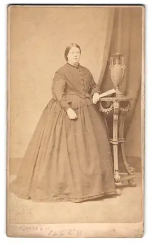 Fotografie Turner & Co., Islington, Upper Street 17, beleibte Dame im Sonntagskleid nebst Tisch & Amphore
