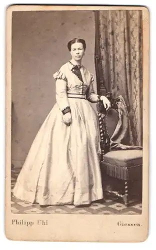 Fotografie Philipp Uhl, Giessen, ältere Dame hellen Kleid mit Aufschlag, stehend am Stuhl
