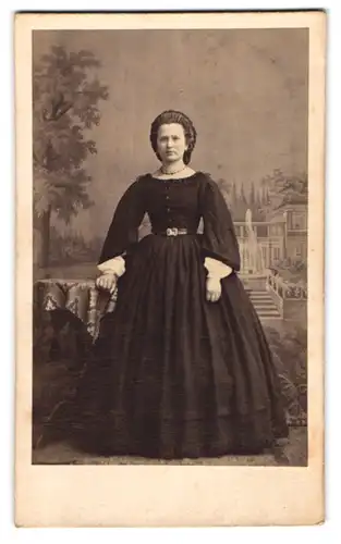 Fotografie H. Wittwer, Neusalz, Portrait junge Dame im dunklen Reifrockkleid mit Perlenkette vor einer Studiokulisse