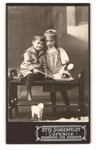 Fotografie Otto Schoenfeldt, Köpenick, Schlossplatz Ecke Schlossstr., Kinderpaar in modischer Kleidung mit Puppe