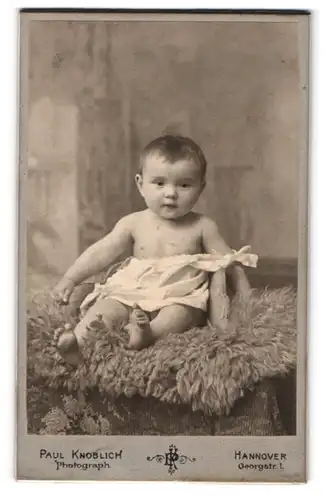 Fotografie Paul Knoblich, Hannover, Georgstrasse 1, Baby in heruntergezogenem Strampelkleidchen auf einem Fell