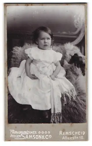 Fotografie Samson & Co., Remscheid, Alleestr. 10, Kleines Mädche im Kleid sitzt auf Fell