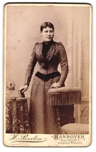 Fotografie H. Barten, Hannover, Georgstr. 1, Portrait junge Frau steht im prachtvollem Kleid an einem Tisch