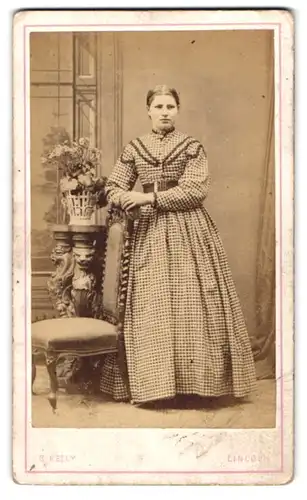 Fotografie B. Kelly, Lincoln, 14. Newland, Frau im Kleid mit Vichy-Muster an Stuhl anlehnend