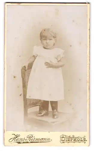 Fotografie Hans Riemann, Diepholz, Kleines Kind im weissen Kleid, auf einem Stuhl stehend