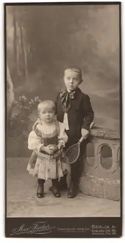 Fotografie Max Fischer, Berlin, zwei junge Kinder im Kleidchen und im Anzug mit Schleife und Tennisschläger