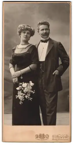 Fotografie William Roth, Berlin, Portrait Paar im Nadelsteifenanzug mit Moustache und im dunklen Kleid mit Perlenkette