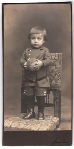 Fotografie Hanns Teich, Berlin, Portrait Kleinkind im Anzug mit Ball in der Hand steht auf einem Stuhl