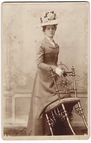 Fotografie unbekannter Fotograf und Ort, Dame mit Hut vor einem Stuhl stehend
