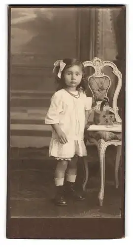 Fotografie unbekannter Fotograf und Ort, niedliches kleines Mädchen im weissen Kleidchen mit Perlenkette und Haarschleife